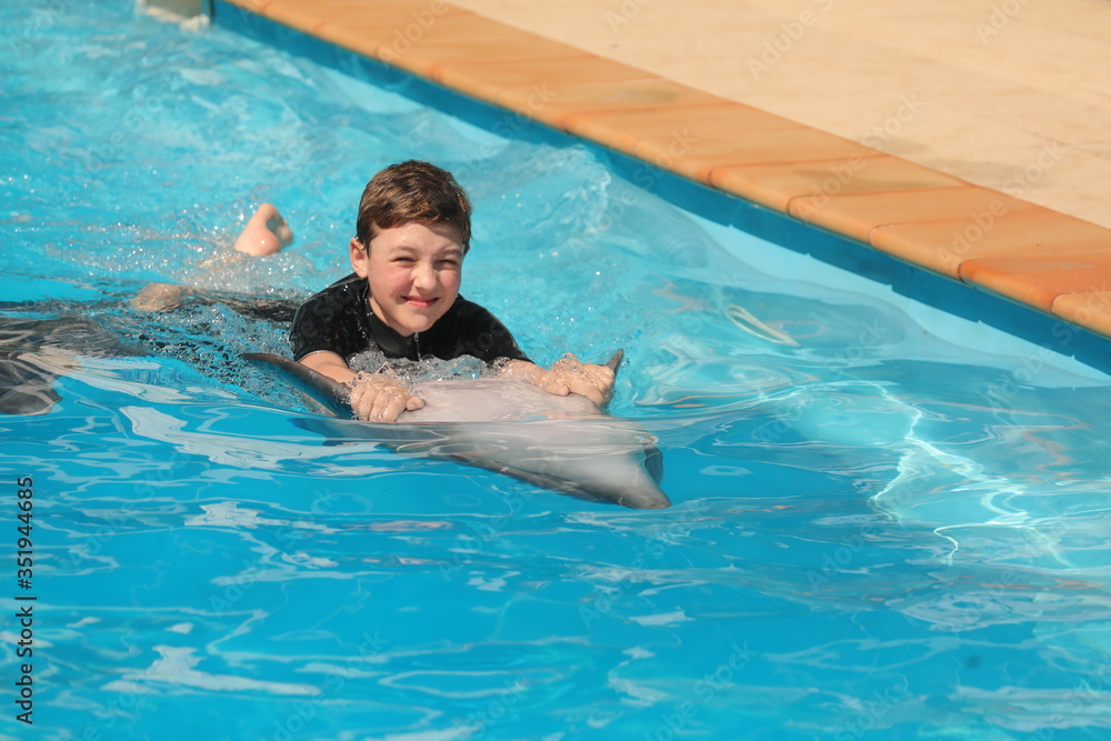  dolphin swims with a boy. the boy is wearing a wetsuit. healthy lifestyle. summer vacation