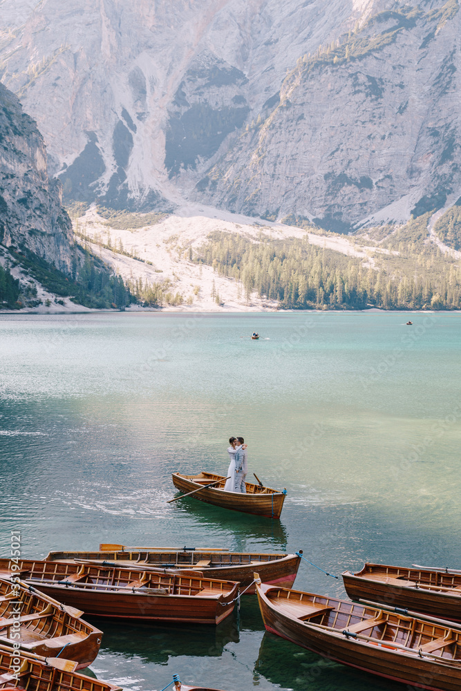 Bride and groom sailing in wooden boat, with oars at Lago di Braies lake in Italy. Wedding in Europe - Newlyweds are standing embracing in a boat.