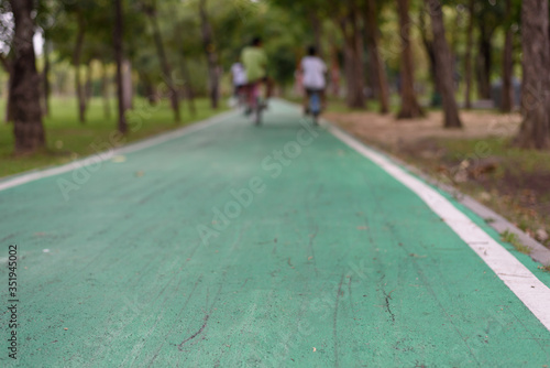 A green cycling lane in a shady park with a blurry background as people are riding a bicycle, copy space