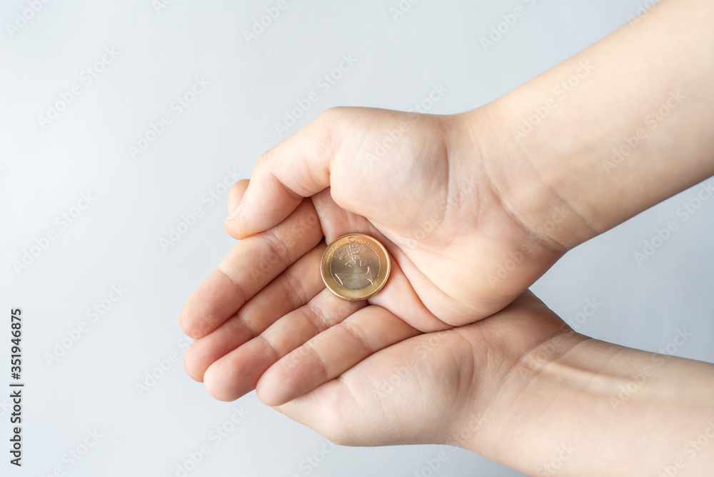 Finance crisis after coronavirus COVID19. Closeup child's hands holding One Euro coin isolated on white background, human hands and saving money concept.
