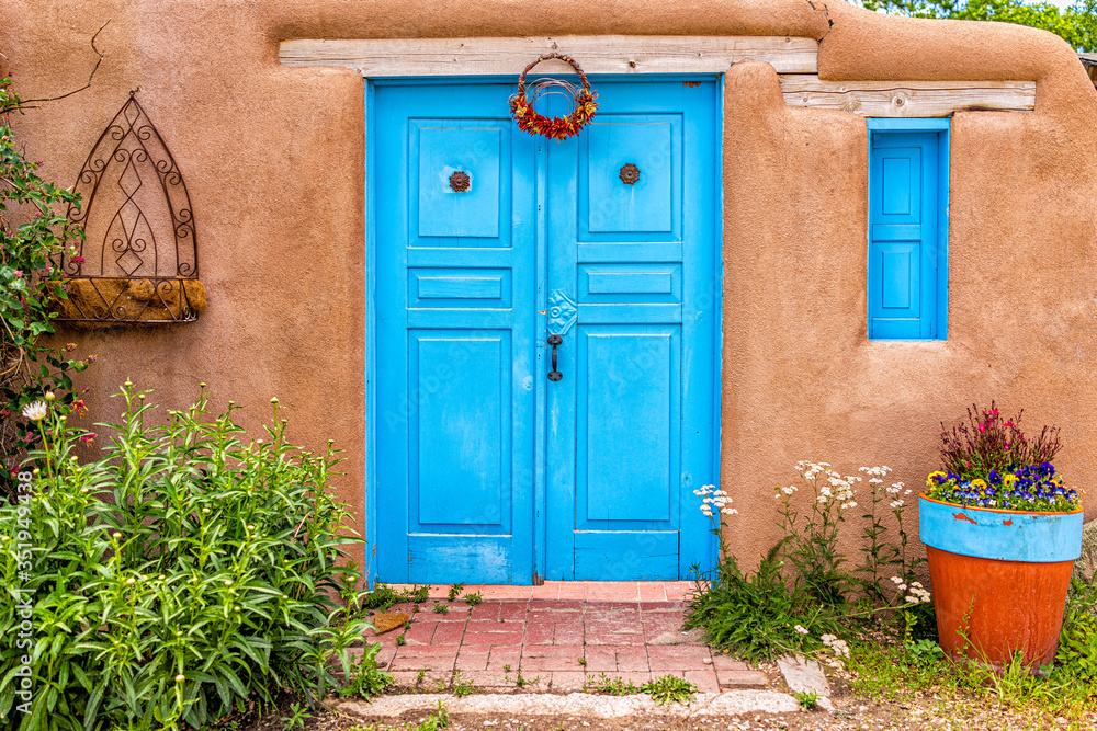 Naklejka premium Tradycyjna kolorowa architektura Nowego Meksyku z niebiesko-turkusowymi kolorami adobe i dekoracjami w ogrodzie przy wejściu