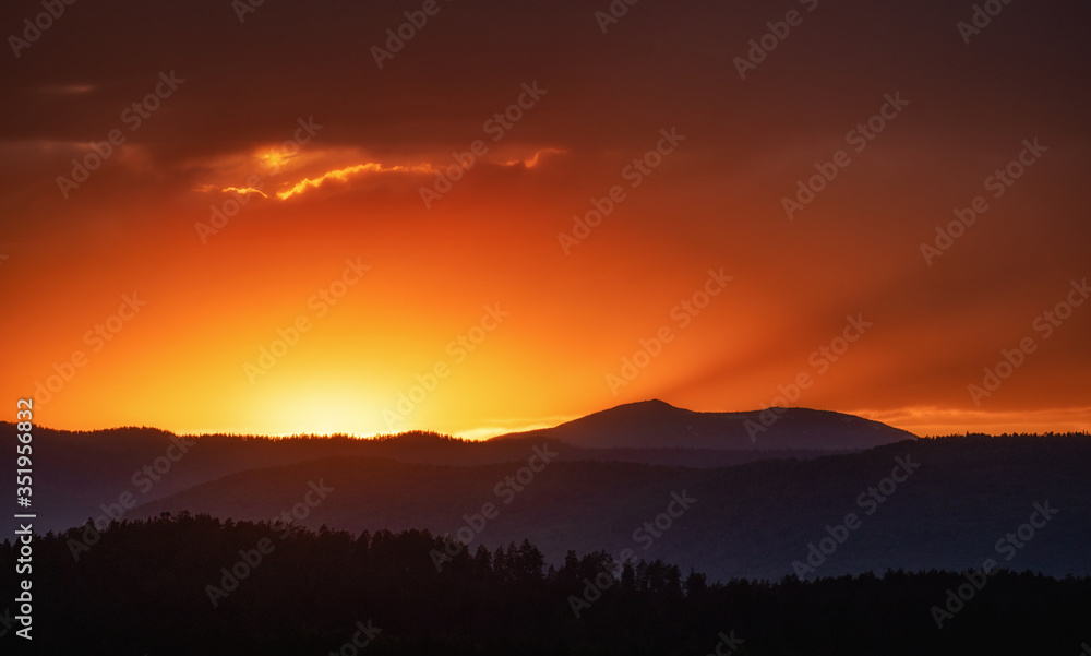 Fototapeta premium Sun setting over hills. Red clouds