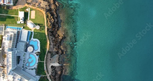 Drone shooting top view of the coastline with luxury hotels or villas with swimming pool, green fresh lawn, its own sandy and rocky beach and calm sea with clear blue water in Larnaca Cyprus.