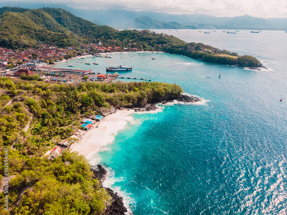 Tropical beach and town in Bali with port, ferry and blue sea. Aerial view