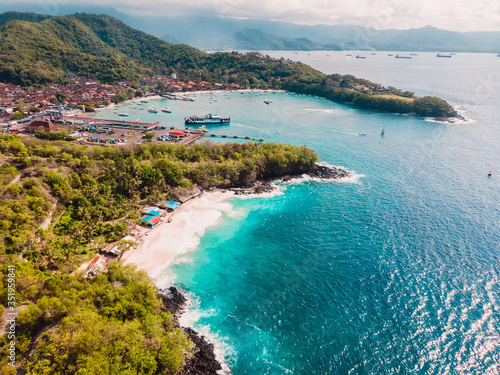 Tropical beach and town in Bali with port, ferry and blue sea. Aerial view