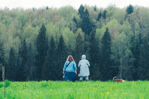 Two beautiful girls with a dog in a meadow in front of a spring forest. Rainy morning. Breakfast with wine in nature.