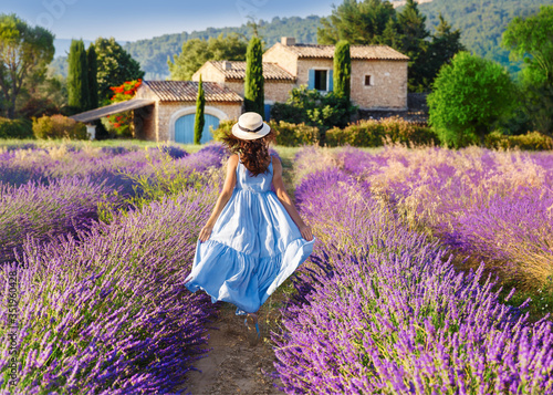 Provence, France. Beautiful view on booming Lavender fields in Provence, France. National park Luberon. Lovely young Caucasian woman enjoying the lavender meadow walking to traditional French house.