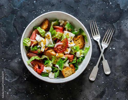 Salad with fresh tomatoes, crunchy ciabatta bread, mozzarella cheese, green salad with olive oil, french mustard, lemon dressing on a dark background, top view