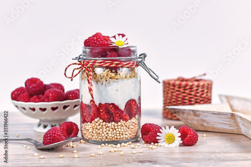 Healthy raspberry fruit dessert with skyr yogurt, granola and puffed quinoa grains layered in jar surrounded by ingredients photo