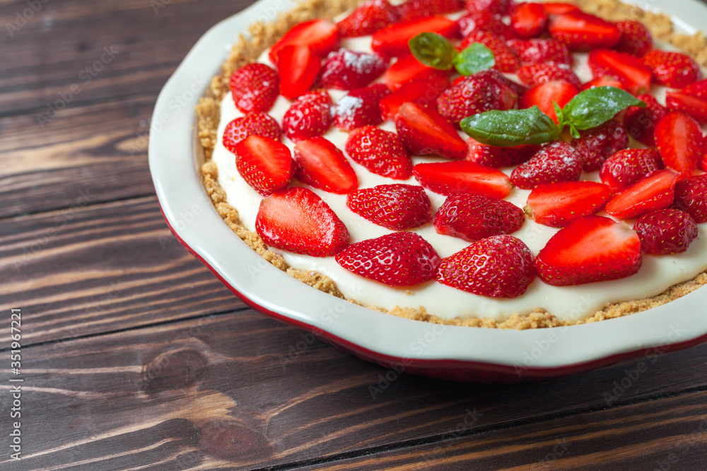 Strawberry cheesecake with basil leaves, in a red ceramic baking dish on a wooden background Strawberry cheesecake with basil leaves, in a red ceramic baking dish on a wooden background