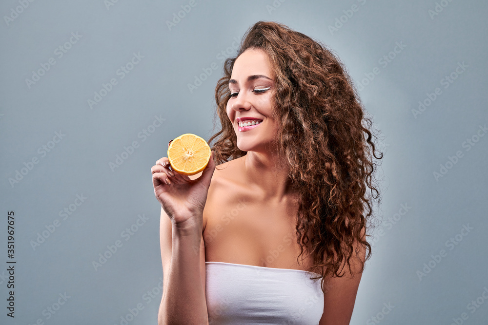 Young happy woman showing a fresh lemon on grey background