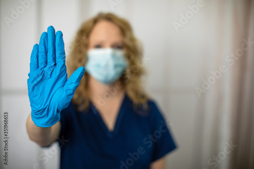 health care worker in scrubs with hand out saying stop now