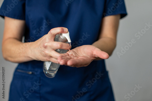 A medical health care worker woman in navy blue scrubs putting antibacterial hand sanitizer on her hands to prevent the spread of germs and disease