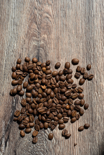 Coffee beans are poured on a wooden surface under sunlight, a fresh, beautiful vertical frame © Aleksey