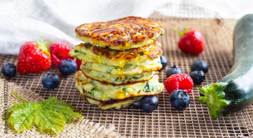 Fresh pile of delicious homemade courgette pancakes topped with honey maple syrup, summer fruits, zucchini and maple leaf on kitchen grill. Close up. Recipe, cooking, season, menu concept