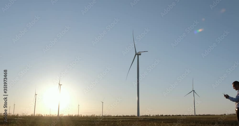 Engineer with a control panel stands on the background of the field of working wind turbines. Engineer with a control panel stands on the background of the field of working wind turbines.