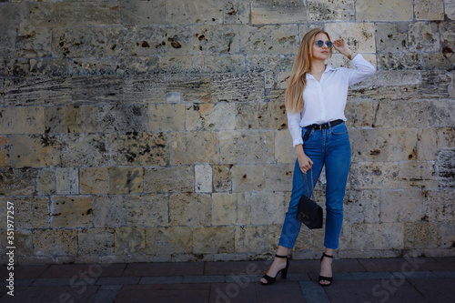 Sunny lifestyle fashion portrait of a young stylish hipster woman walking in the city, wearing a fashionable outfit
