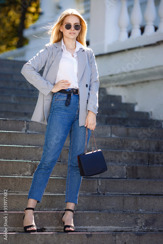 Sunny lifestyle fashion portrait of a young stylish hipster woman walking in the city, wearing a fashionable outfit
