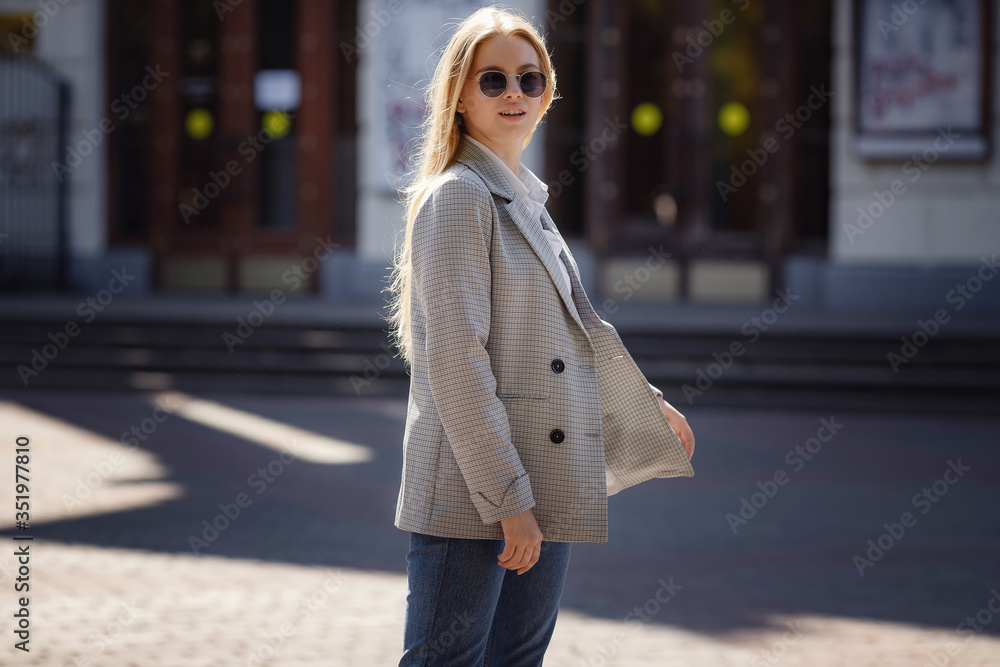 Fototapeta premium Sunny lifestyle fashion portrait of a young stylish hipster woman walking in the city, wearing a fashionable outfit