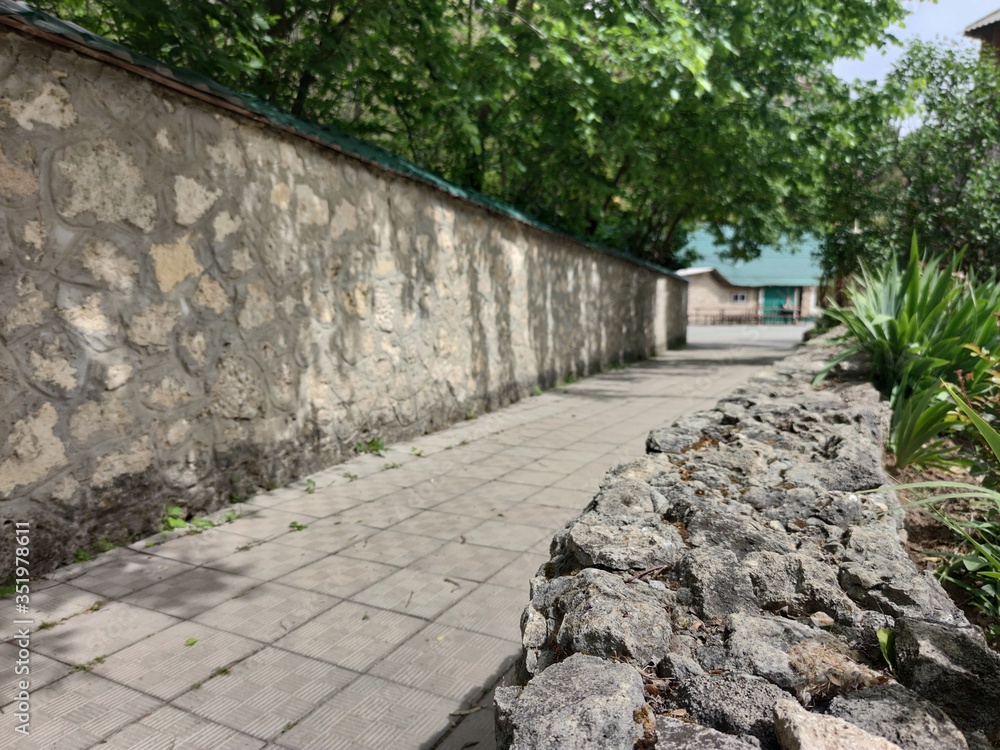 The stone wall of an Orthodox monastery. Green plants, Stone steps. Blue sky. The stone wall of an Orthodox monastery. Green plants, Stone steps. Blue sky.