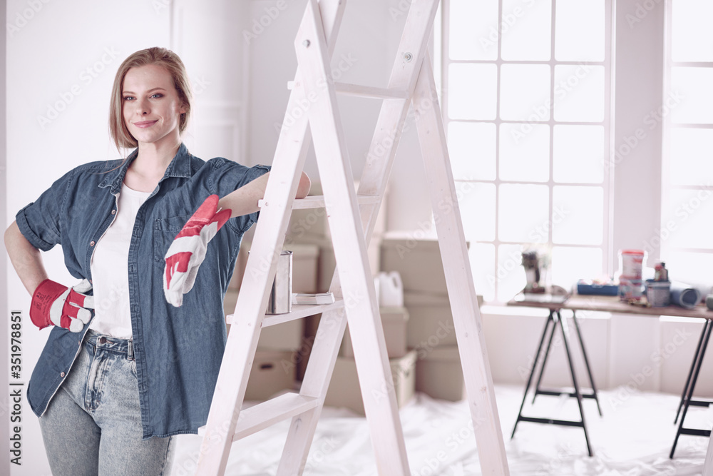 Beautiful young woman on a white wooden stepladder. Ready to repair the room. Women housework concept Beautiful young woman on a white wooden stepladder. Ready to repair the room. Women housework concept