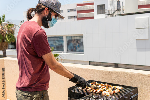 Man is barbequing in the terrace with a mask due covid 19