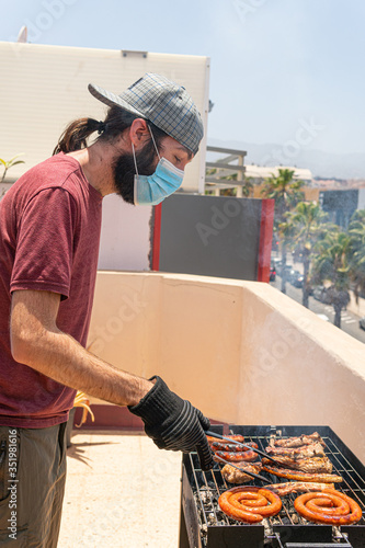 Man is barbequing in the terrace with a mask due covid 19