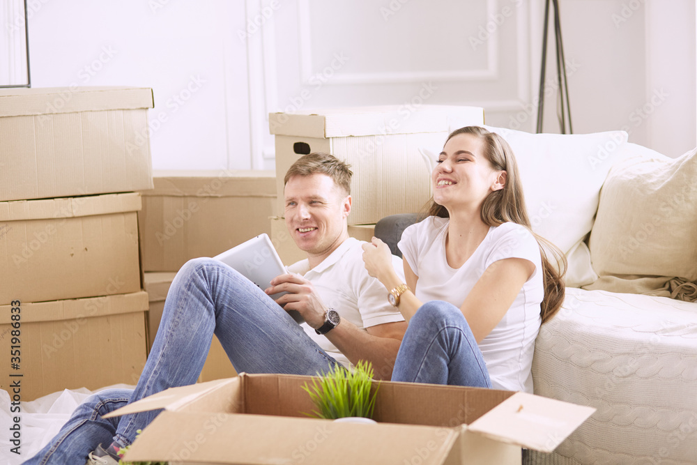 Portrait of happy couple looking at laptop computer together sitting in new house, surrounded with boxes Portrait of happy couple looking at laptop computer together sitting in new house, surrounded with boxes