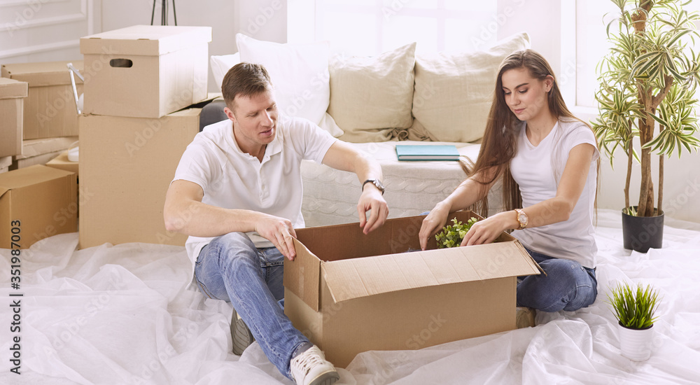 Portrait of happy couple looking at laptop computer together sitting in new house, surrounded with boxes Portrait of happy couple looking at laptop computer together sitting in new house, surrounded with boxes