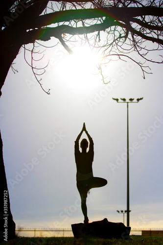 Silhouette of a woman practising yoga in the sun in a park.