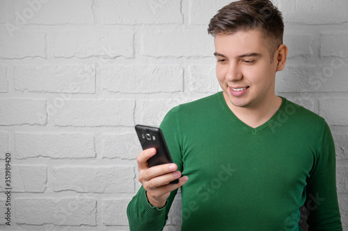 Happy man checking smart phone content. Brick wall background. Studio photo.