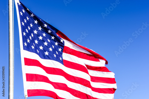 American flag is flowing in the wind on blue sky background.