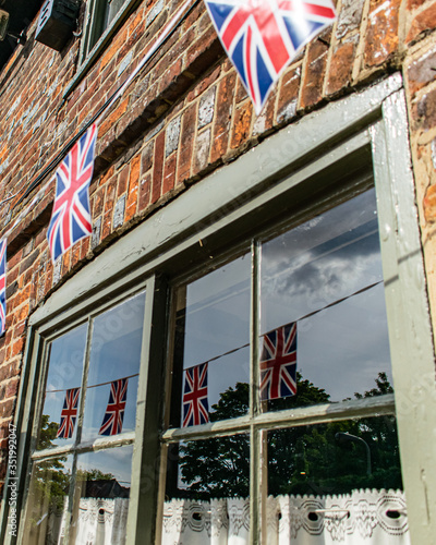 Union Jack bunting on a building, many flags in row on a string, reflection in the window of VE day decorations in UK, memorial symbol of winning second world war, english patiotic view photo