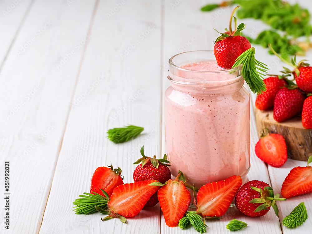 Strawberry cocktail in a glass jar on a wooden white table. Strawberries and spruce tips, smoothie ingredients scattered on the table. Close-up with copy space. Strawberry cocktail in a glass jar on a wooden white table. Strawberries and spruce tips, smoothie ingredients scattered on the table. Close-up with copy space.