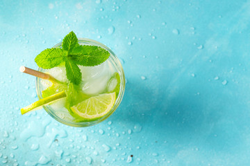 Homemade lemonade or mojito cocktail with lime, mint and ice cubes in a glass on a light stone table. Fresh summer drink. Top view with copy space.