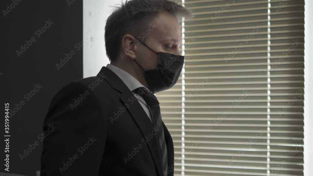 Business during COVID 19 pandemic. Young businessman in business suit stands near window closed by shutters and looks in sadness at the street. How to save a business in quarantine period concept. Business during COVID 19 pandemic. Young businessman in business suit stands near window closed by shutters and looks in sadness at the street. How to save a business in quarantine period concept.