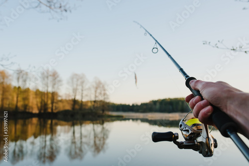 Fisherman with rod throws bait into the water on river bank. Fishing for pike, perch. Background wild nature. Concept of rural getaway. Man catching a fish on lake or pond with text space. Fishing day