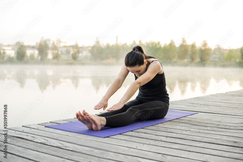 Young brunette sportswoman stretching training outside on violette yoga mat. Healthy active life concept
