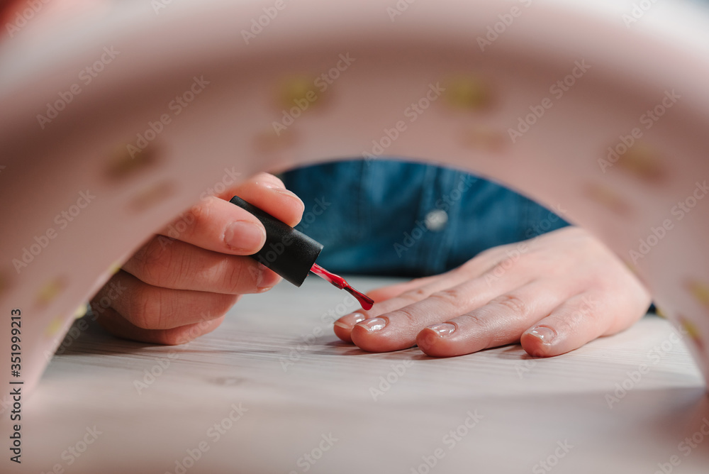 Girl makes a manicure at home. Woman doing manicure herself, draws, paints a brush, gel nail polish. Home life during quarantine, coronavirus pandemic, self-isolation. UV lamp with light. Girl makes a manicure at home. Woman doing manicure herself, draws, paints a brush, gel nail polish. Home life during quarantine, coronavirus pandemic, self-isolation. UV lamp with light.