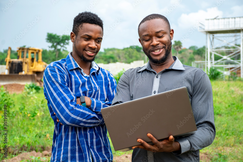 african agricultural business men, discussing using a laptop on a piece of land african agricultural business men, discussing using a laptop on a piece of land