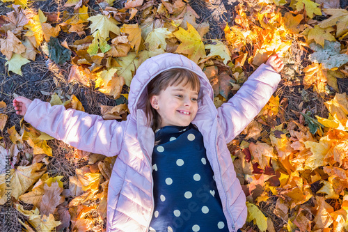 Happy girl 7-8 years old  playing in the park  lying on the yellow autumn leaves on a sunny day  park background at golden hour.
