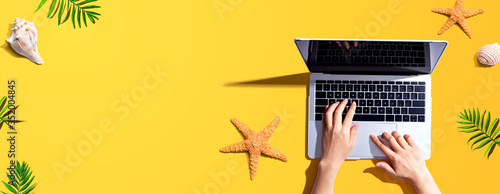 Person using a laptop computer with summer theme objects - flat lay