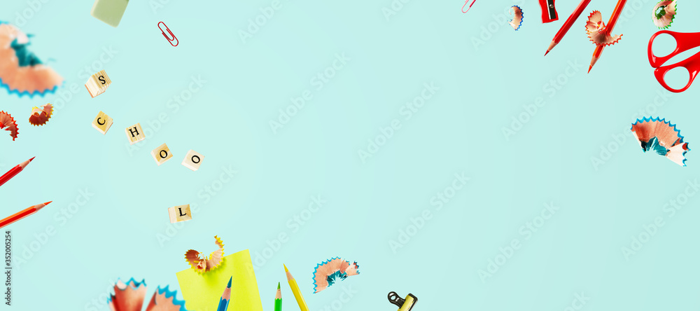 Creative back to school background with flying pencil shavings, wooden letter seals on a blue background with copy space. The letters are grouped into the word SCHOOL. Banner.