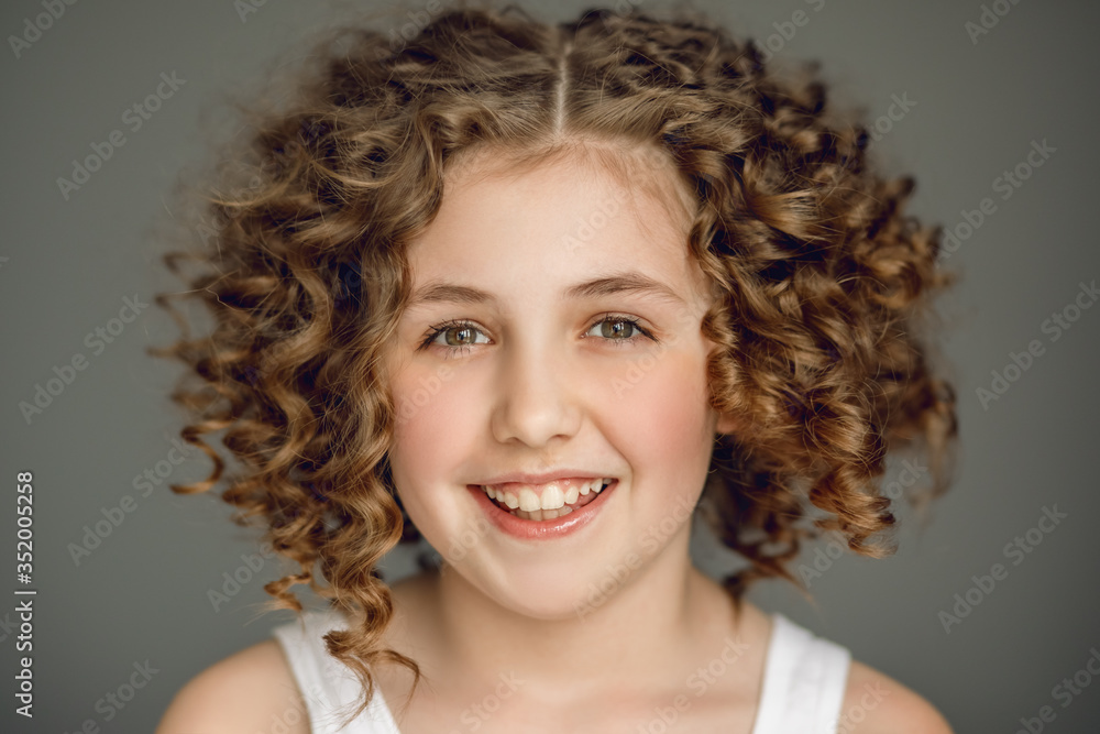 Close-up portrait. Teen girl with curly hair smiles beautifully. The vzgyad directs directly into the frame. Gray background. Emotions joy. Delight, smile, even teeth. Close-up portrait. Teen girl with curly hair smiles beautifully. The vzgyad directs directly into the frame. Gray background. Emotions joy. Delight, smile, even teeth.