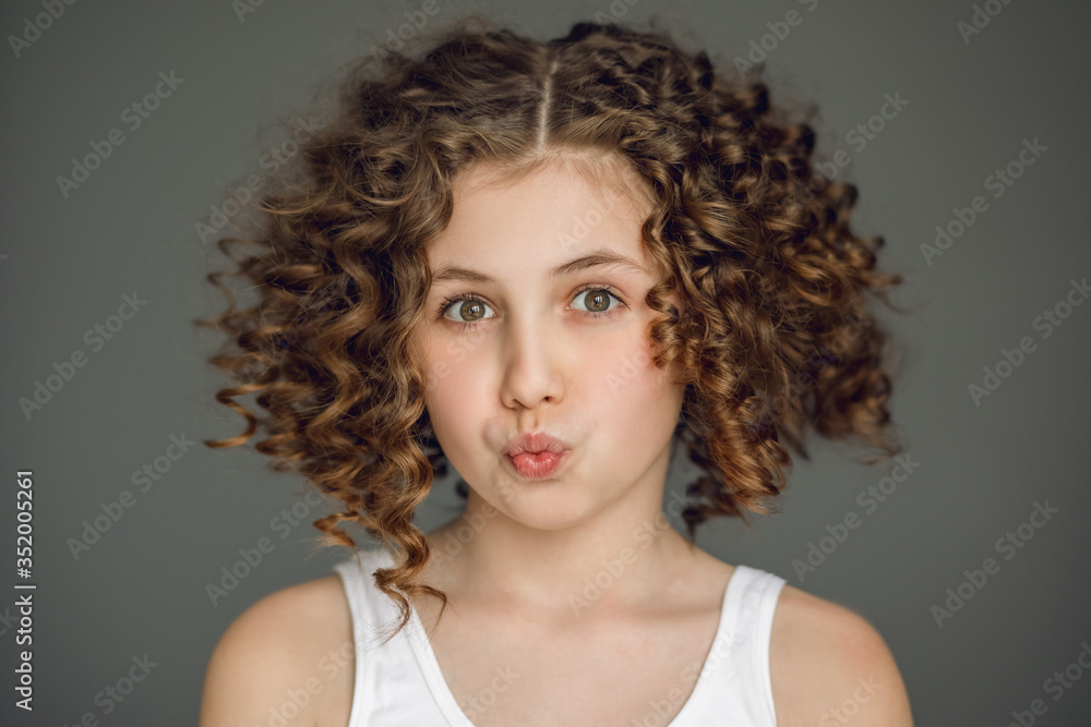 Close-up portrait. A teenage girl with curly hair curled her lips into a tube. The vzgyad directs directly into the frame. Gray background. Emotion surprise, joy, delight, smile, straight teeth. Close-up portrait. A teenage girl with curly hair curled her lips into a tube. The vzgyad directs directly into the frame. Gray background. Emotion surprise, joy, delight, smile, straight teeth.