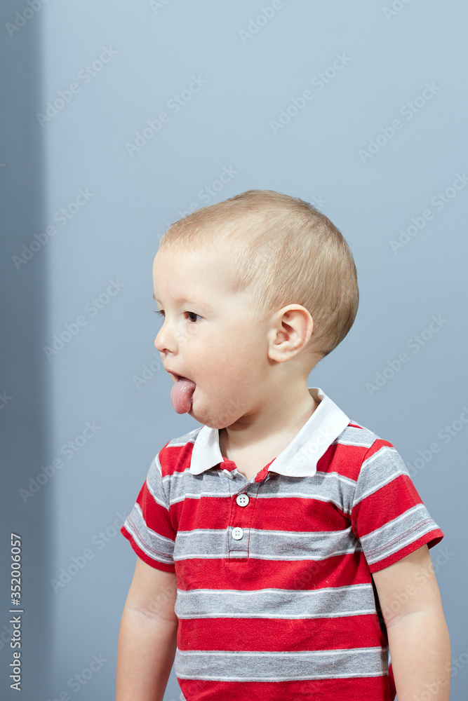 Little kid shows tongue on a light background
