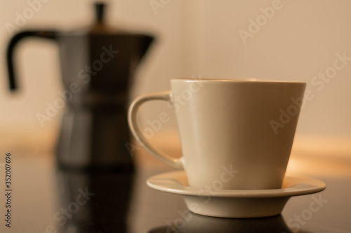 Coffee cup with a coffee maker in the background and out of focus