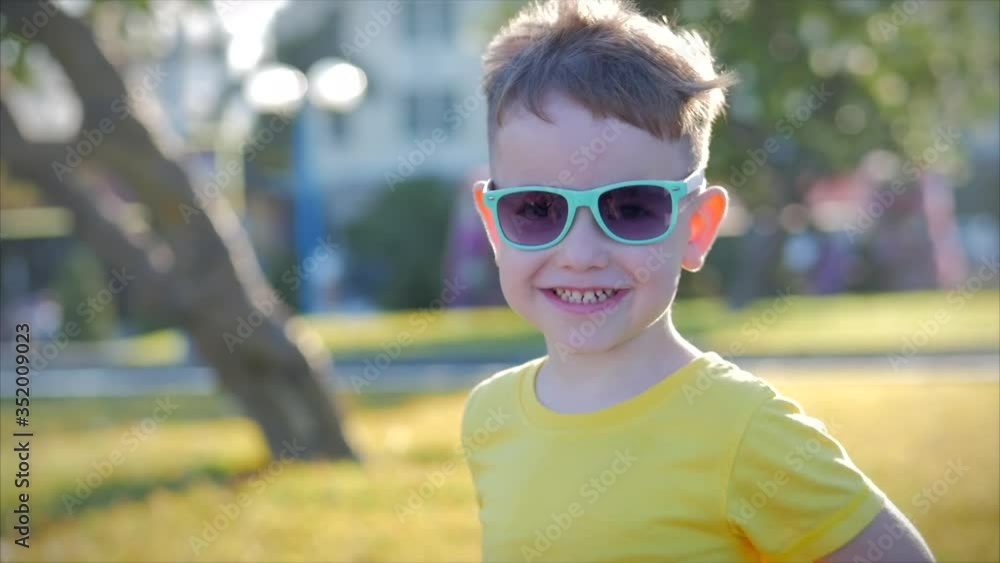 Portrait of a funny little boy in sunglasses and looking at camera smiles, beautiful smile, sunny summer day, cute baby face of preschooler, looking at camera on the street. Portrait of a funny little boy in sunglasses and looking at camera smiles, beautiful smile, sunny summer day, cute baby face of preschooler, looking at camera on the street.