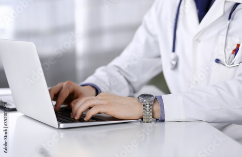 Unknown male doctor sitting and working with laptop in clinic at his working place  close-up. Young physician at work. Perfect medical service  medicine concept