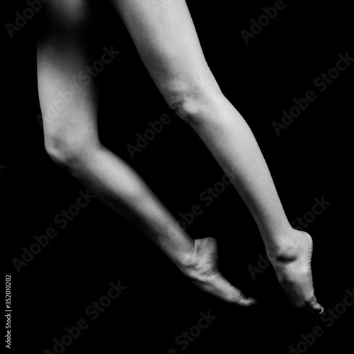 black and white photo of female legs standing on bent fingertips isolated on black background